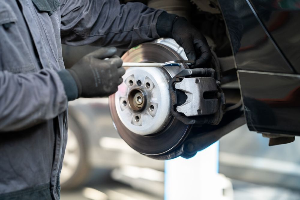 Mechanic working on car brake system, using a wrench.