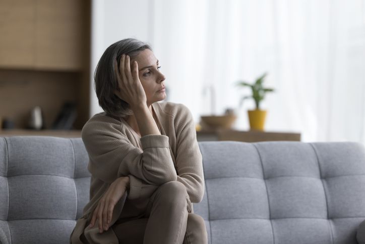 Sad thoughtful grey haired woman sitting on sofa at home stock photo.