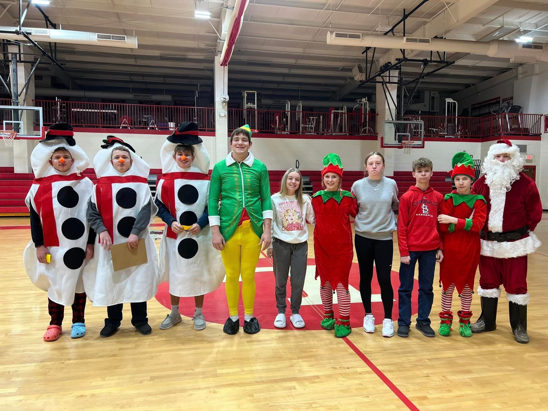 Group of children in festive costumes pose in a gymnasium, including dice, elf, snowman, and Santa.