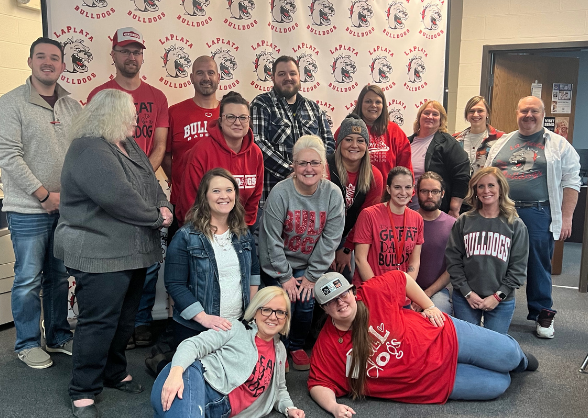 Group of people in red shirts pose in front of a banner, smiling.
