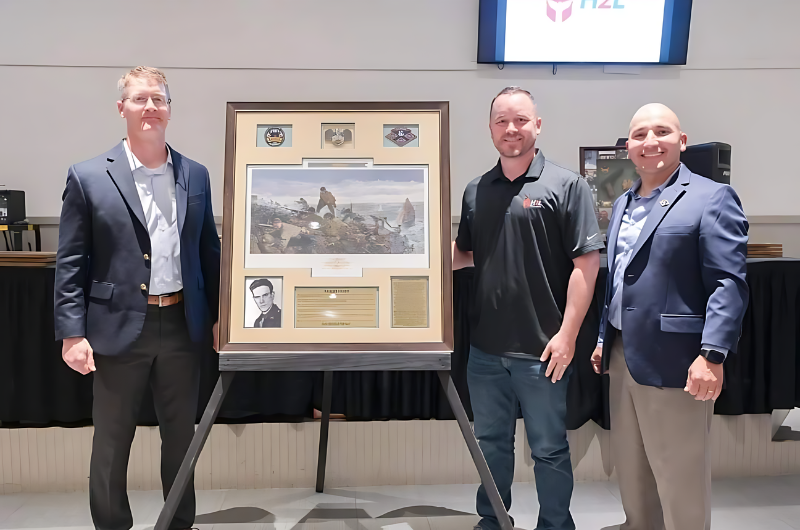 Three men are standing in front of a framed picture.