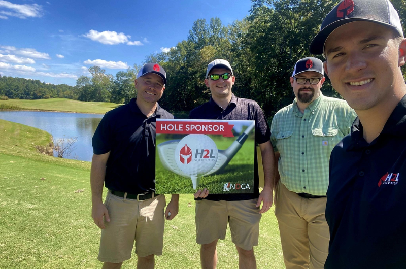 A group of men are standing on a golf course holding a sign.