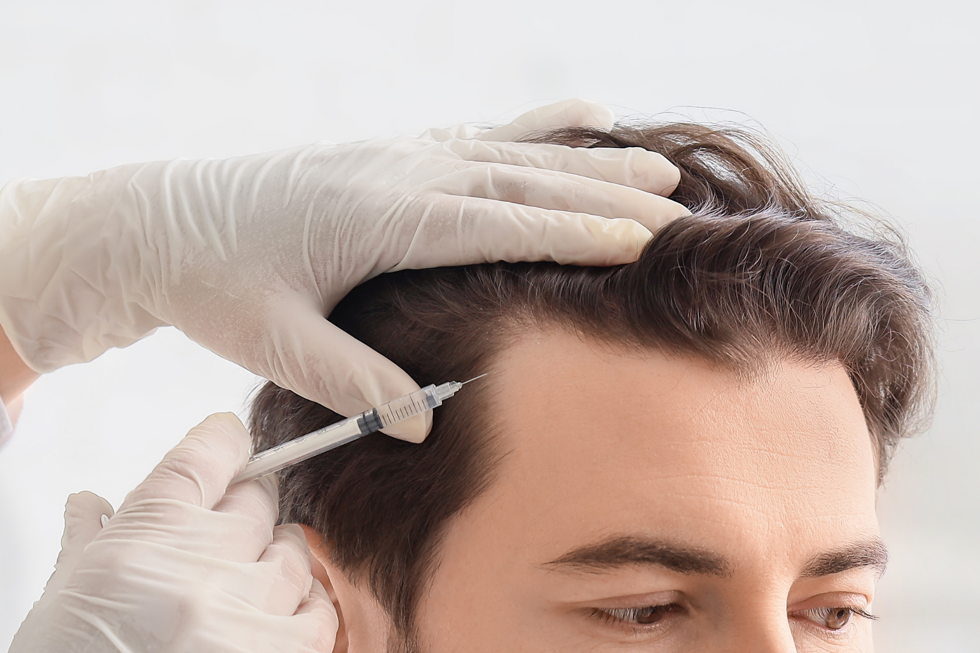 Doctor examines a man's face with a medical instrument; both are wearing gloves, mask and lab coat.