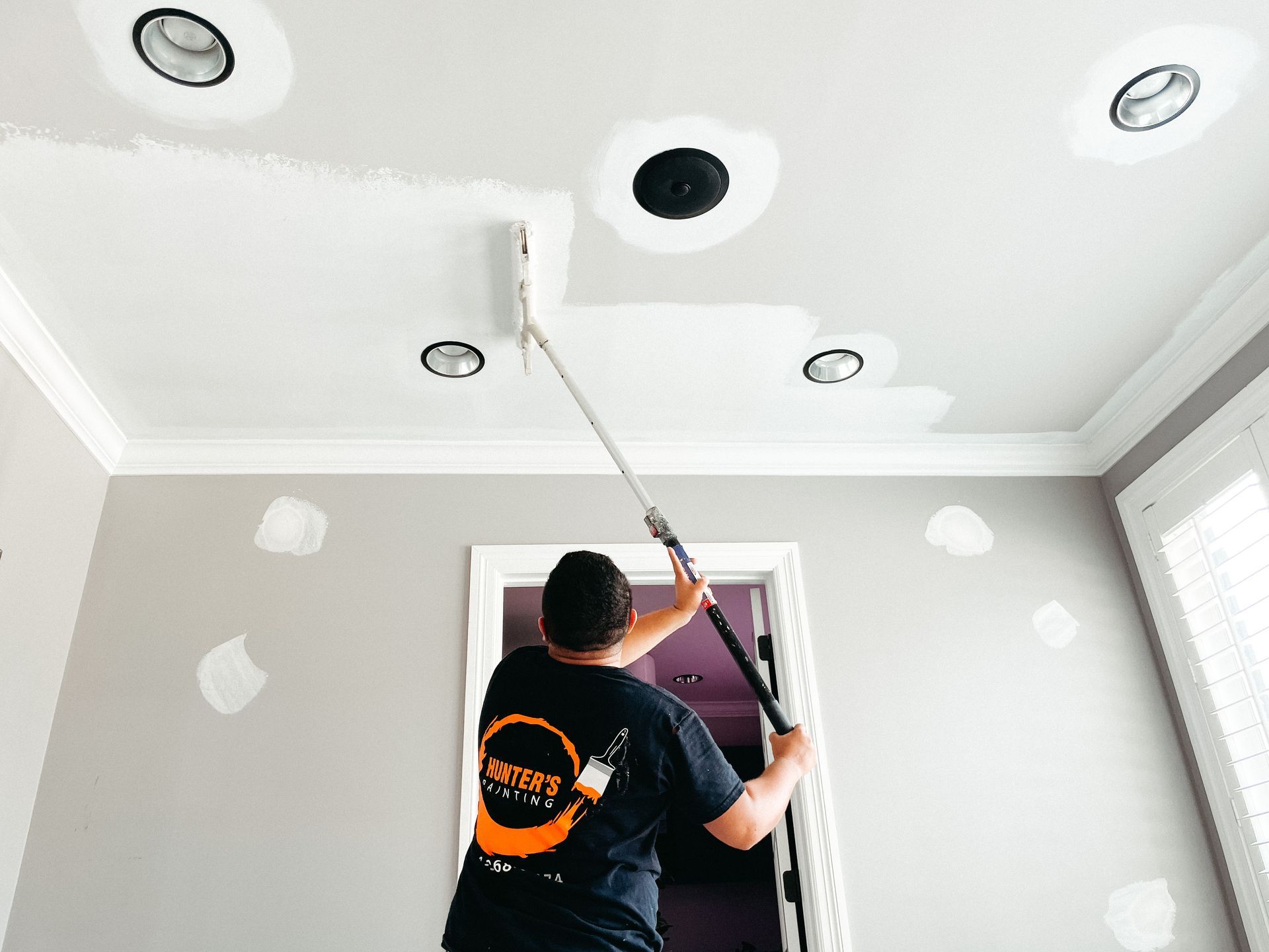 A man is painting the ceiling of a room with a paint roller.