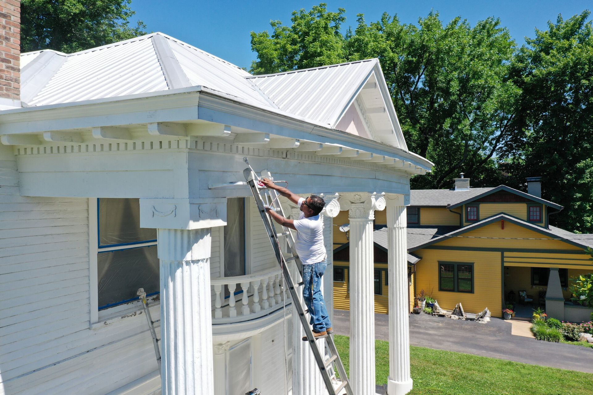 A man on a ladder paints the roof of a house