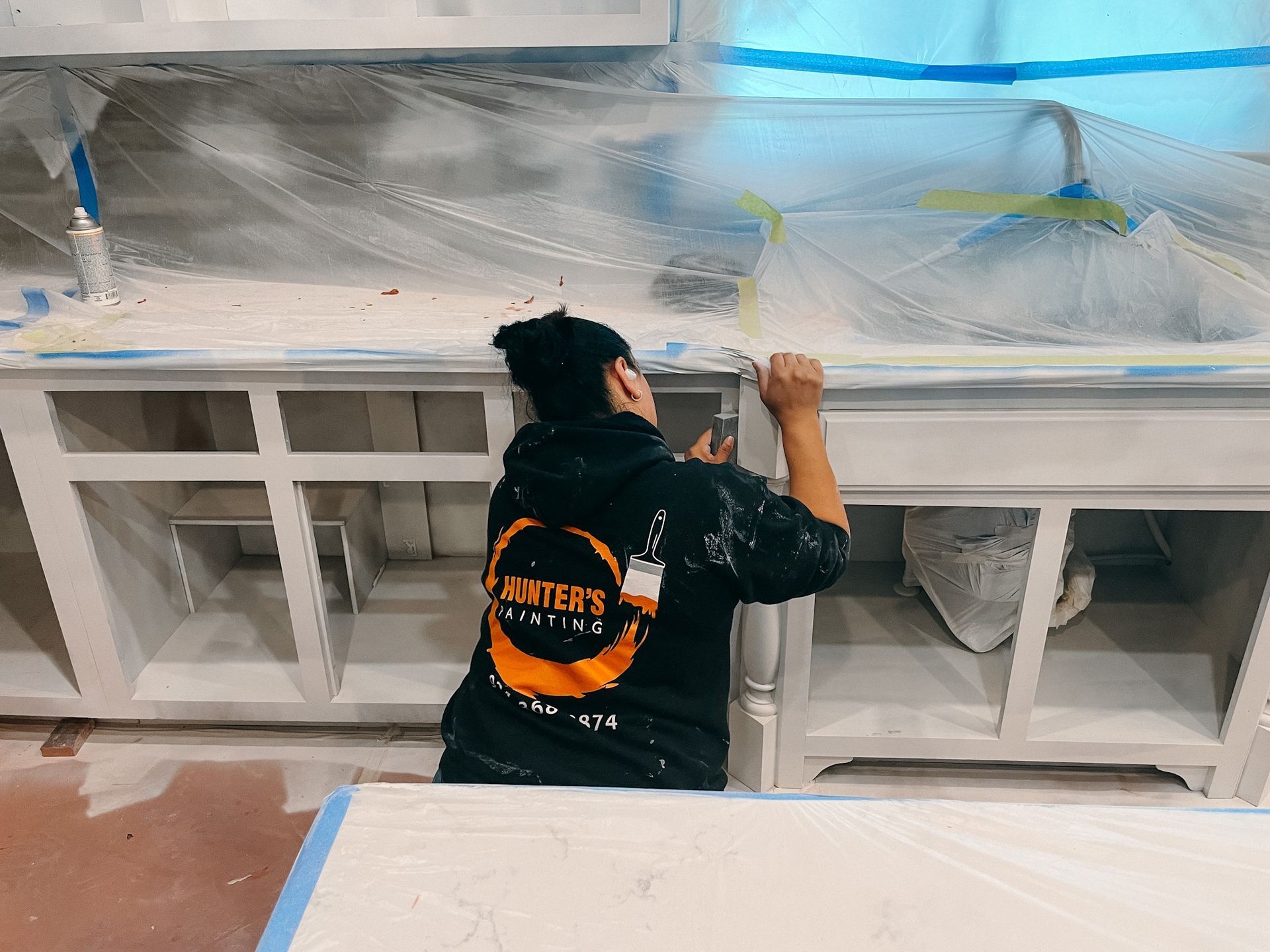 A man is painting a kitchen counter with white paint.
