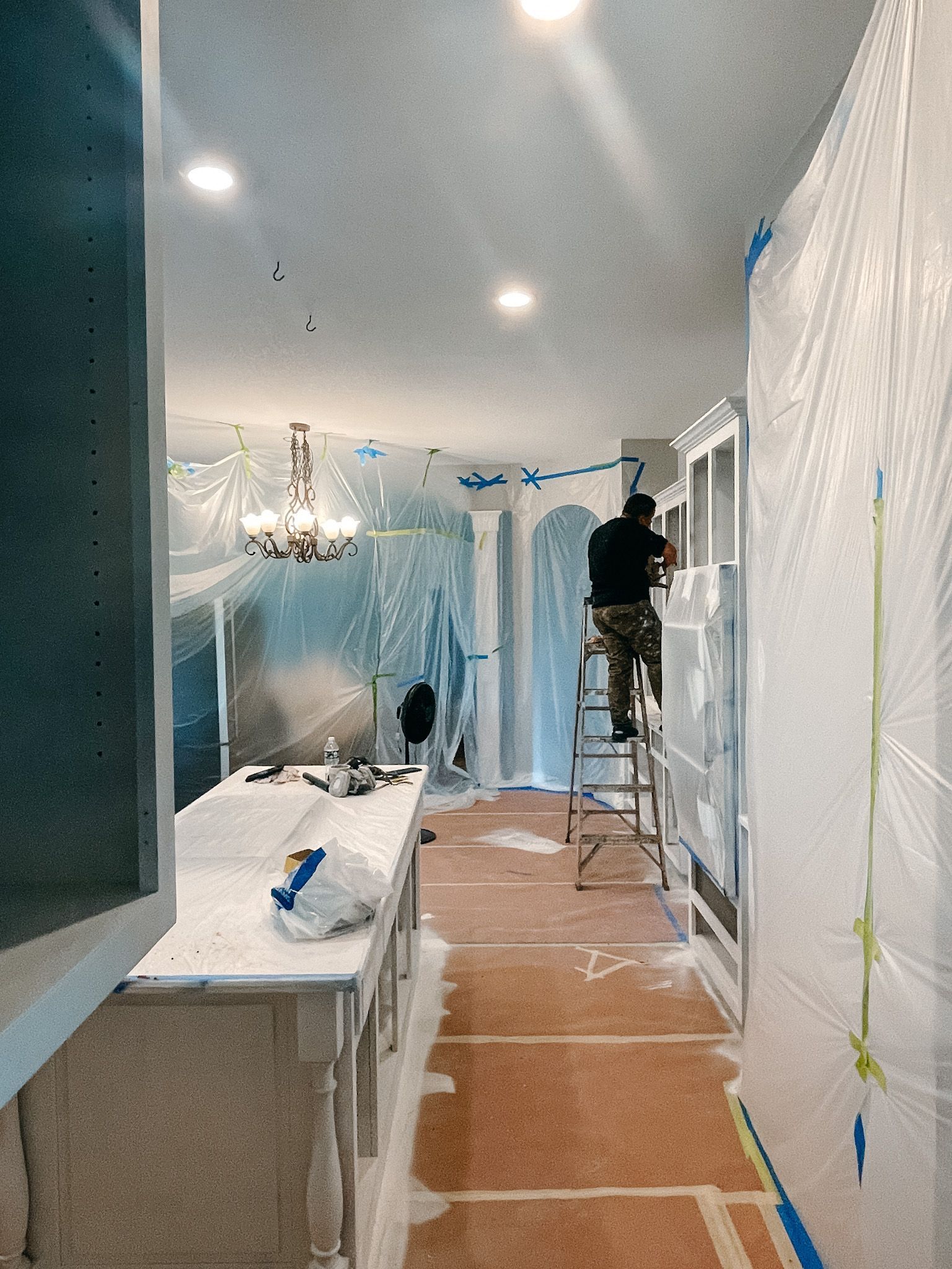 A man is standing on a ladder painting a wall in a bathroom.