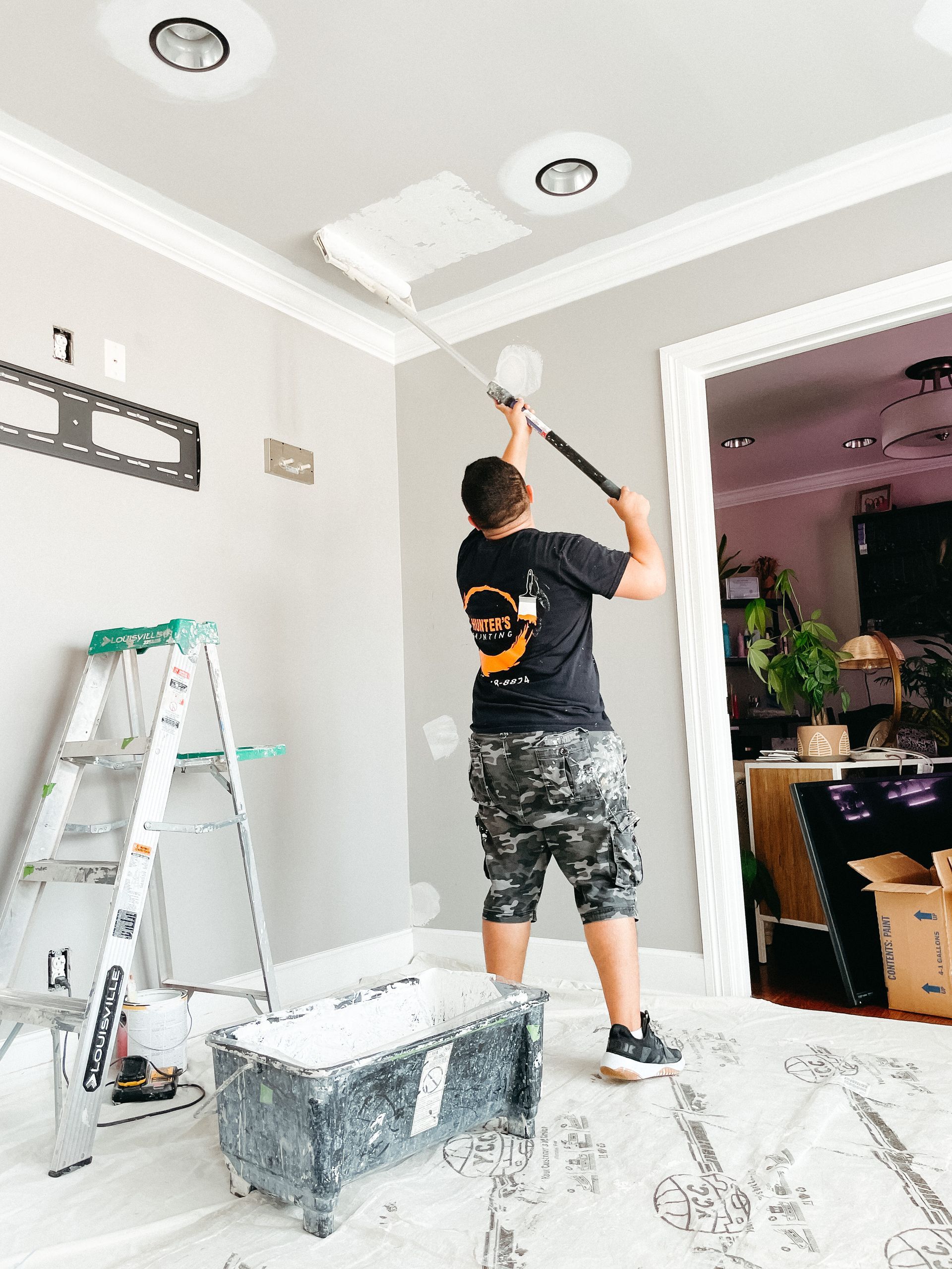 A man is painting the ceiling of a room with a paint roller.