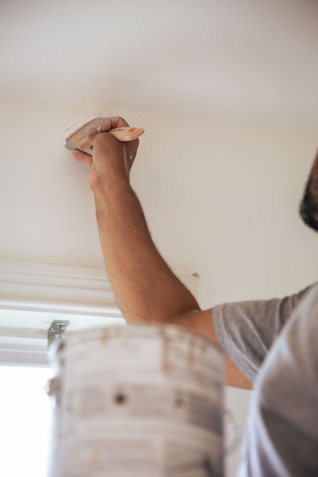 A man is painting the ceiling with a brush.