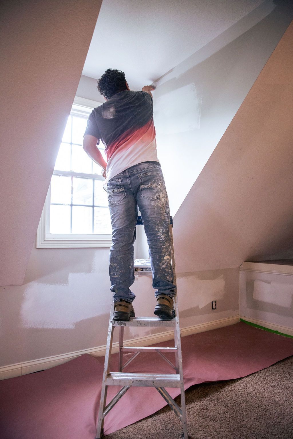 A man is standing on a ladder painting a wall.