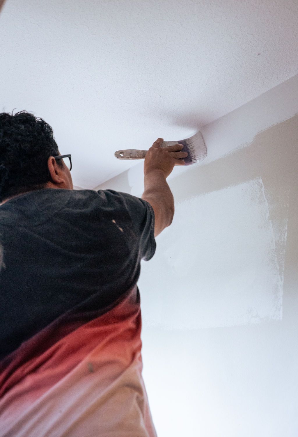 A man is painting the ceiling with a brush.