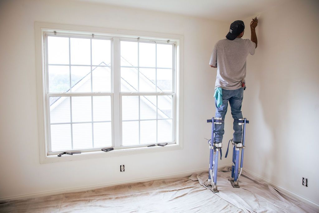 A man is standing on a ladder in an empty room painting a wall.