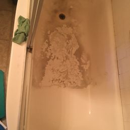 A white bathtub with significant damage, showing peeling and worn-away finish near the drain.