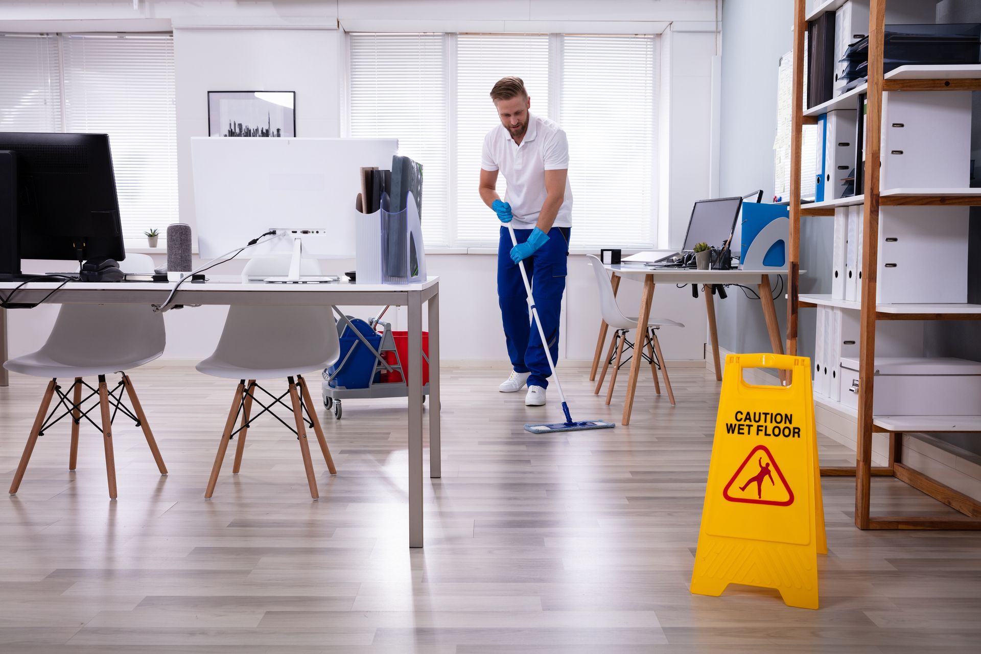 A cleaner mops the floor of an office near a yellow 