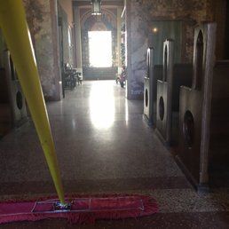 A long-handled dust mop with a red head rests on the shiny, polished floor of a hallway lined with wooden pews.