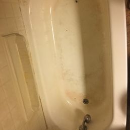 A top-down view of an off-white bathtub with visible stains and grime on the basin floor and surrounding tiled walls.