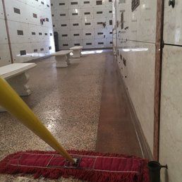 A yellow-handled red dust mop sweeps the floor of a marble mausoleum with rows of burial niches.