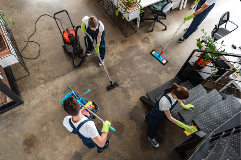 Four people in uniforms cleaning the floors and stairs of a modern office space.