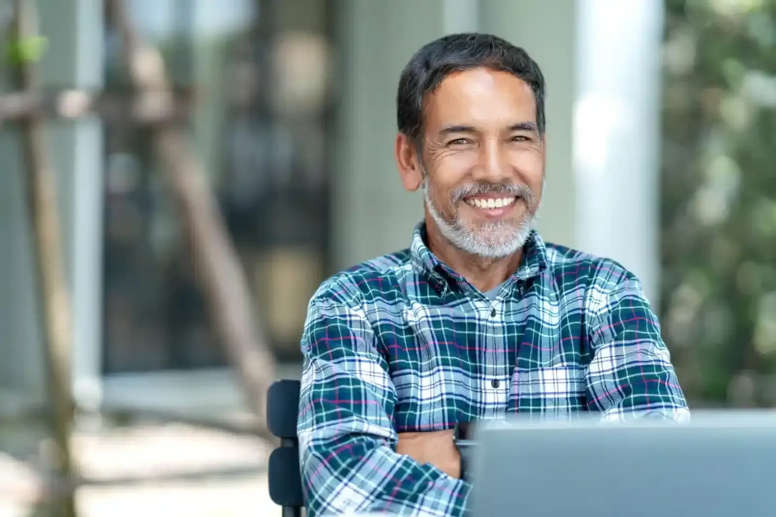 A man in a plaid shirt is sitting in front of a laptop computer.