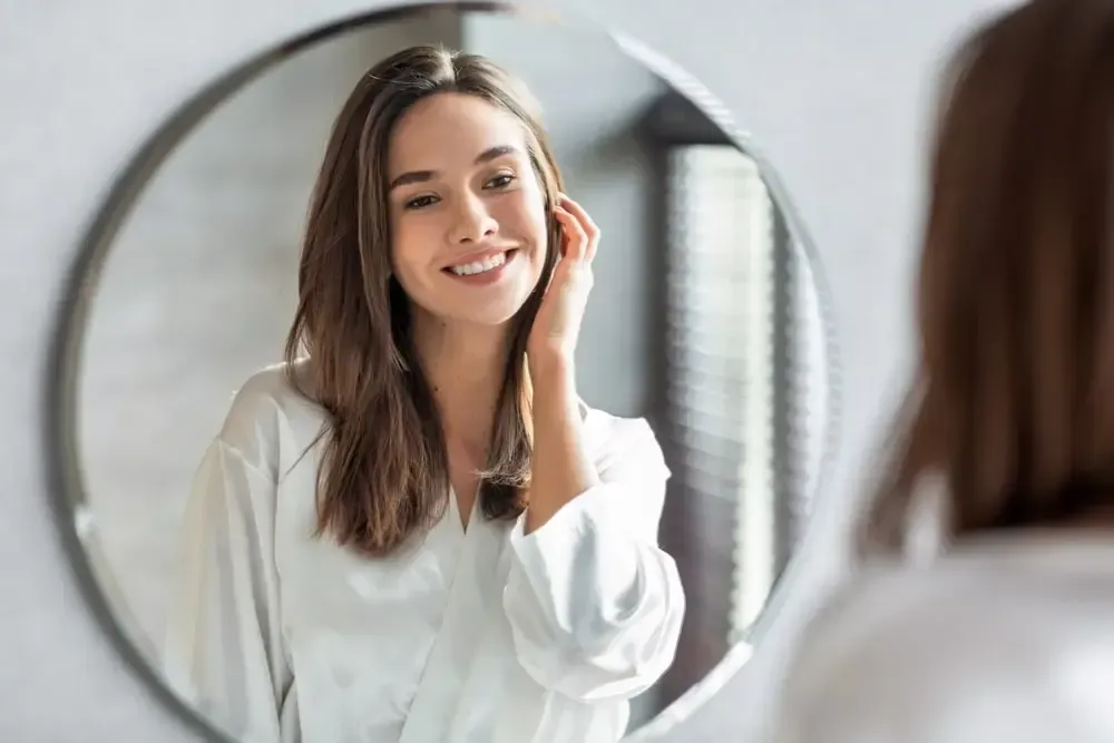 A woman is smiling while looking at herself in the mirror.