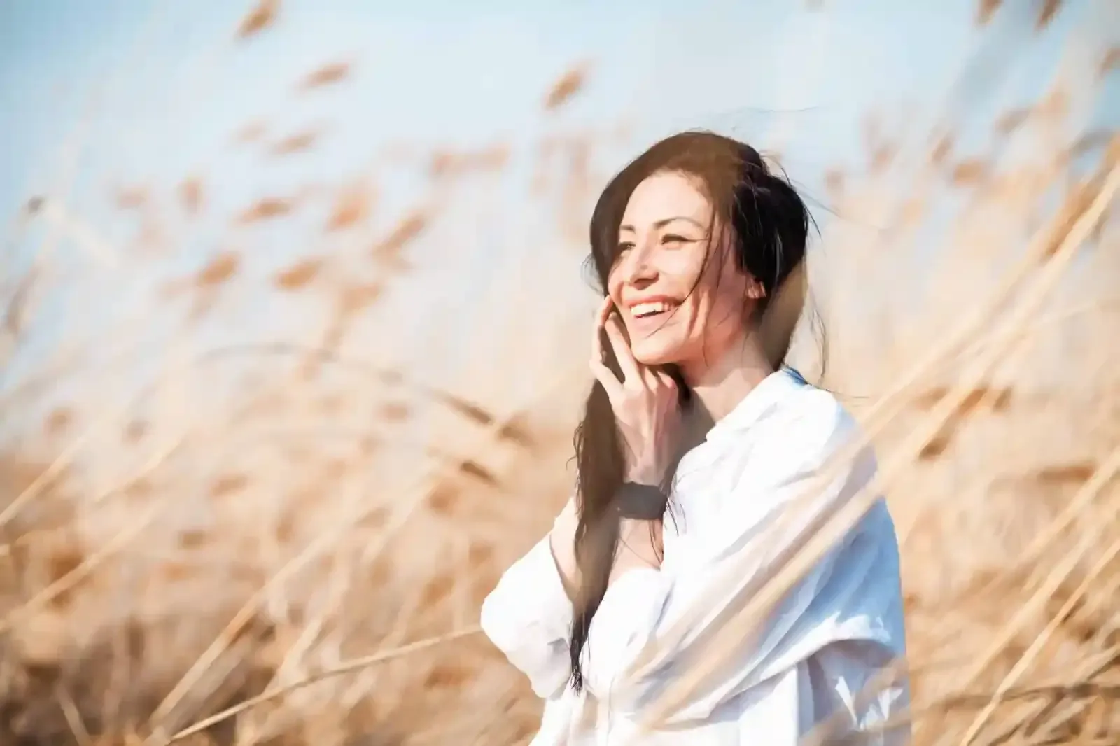 A woman is standing in a field of tall grass talking on a cell phone.
