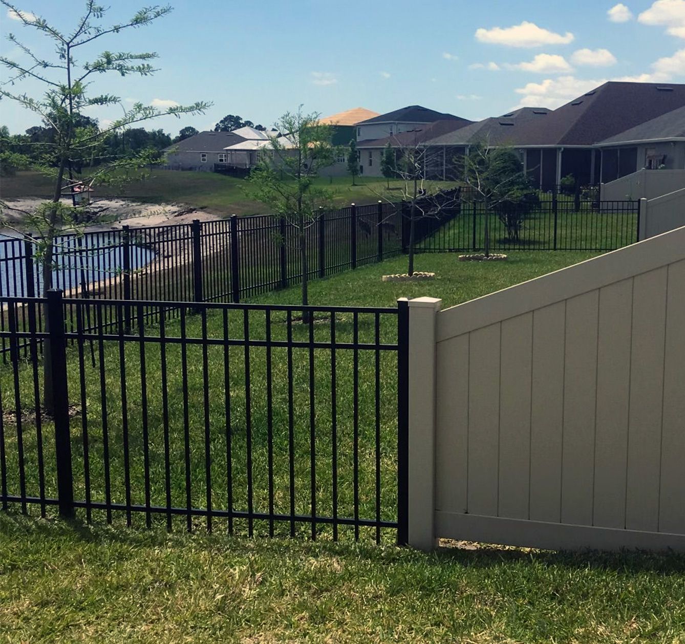 A white fence surrounds a lush green yard with houses in the background