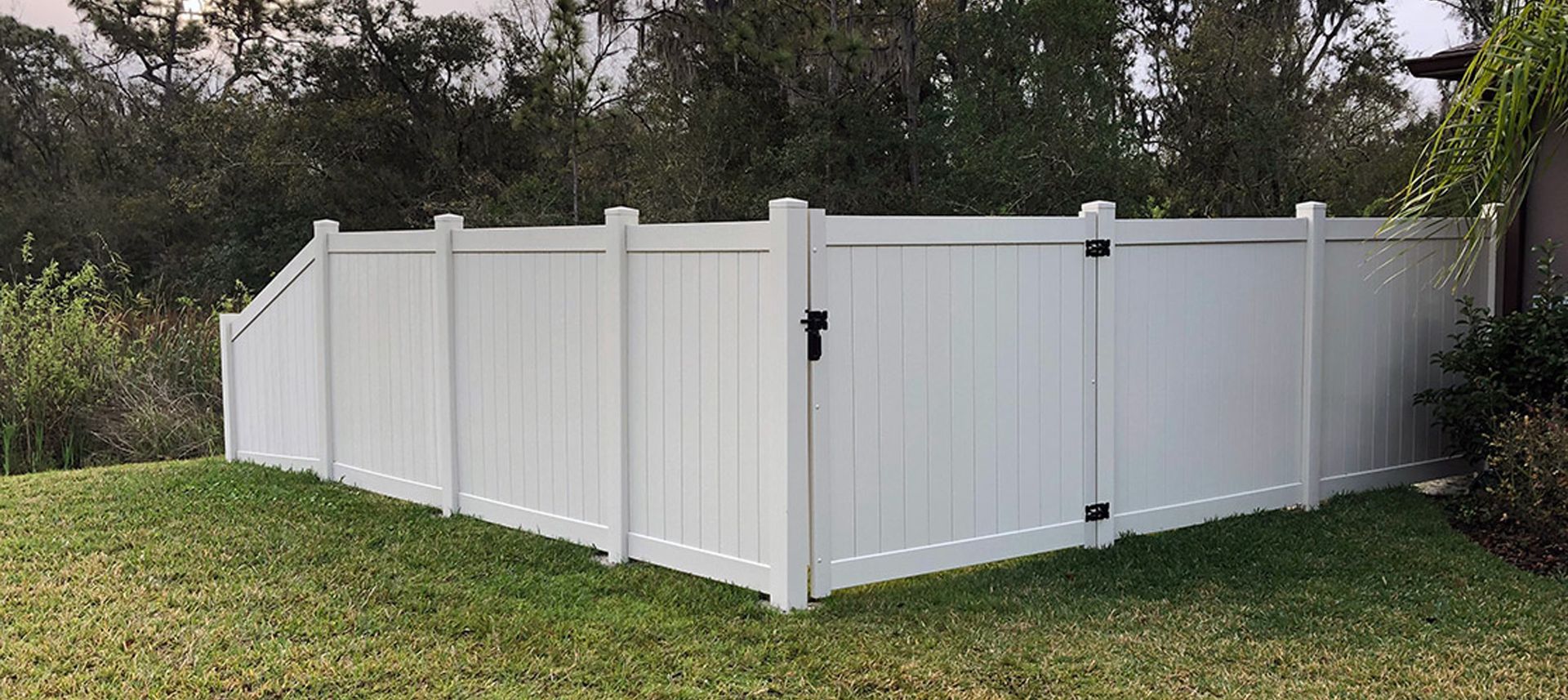 A white vinyl fence with a black gate is sitting on top of a lush green lawn.