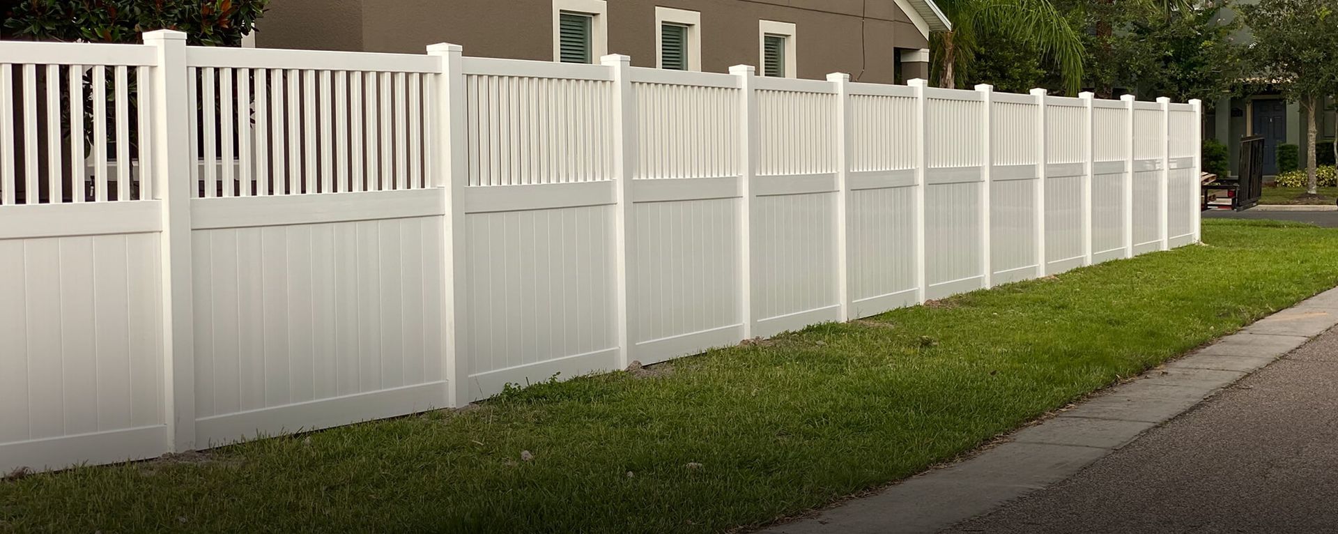 A white vinyl fence surrounds a lush green yard in front of a house.