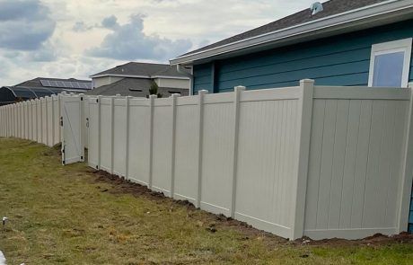 A white vinyl fence is surrounding a blue house.