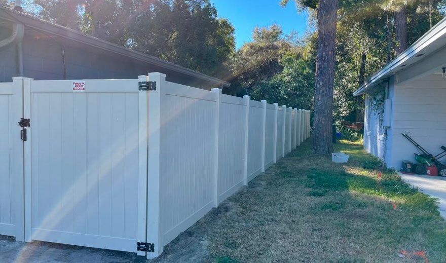 A white vinyl fence with a gate in the backyard of a house.