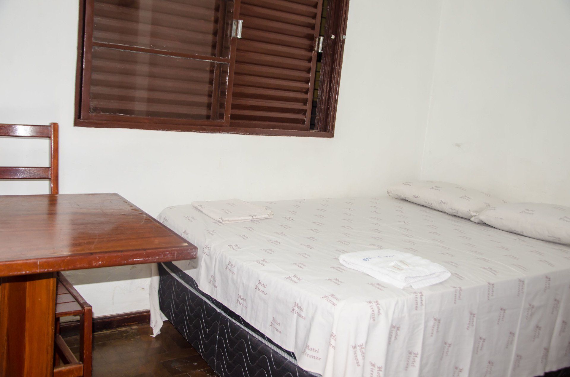 Um quarto com uma cama, mesa, cadeira e janela.