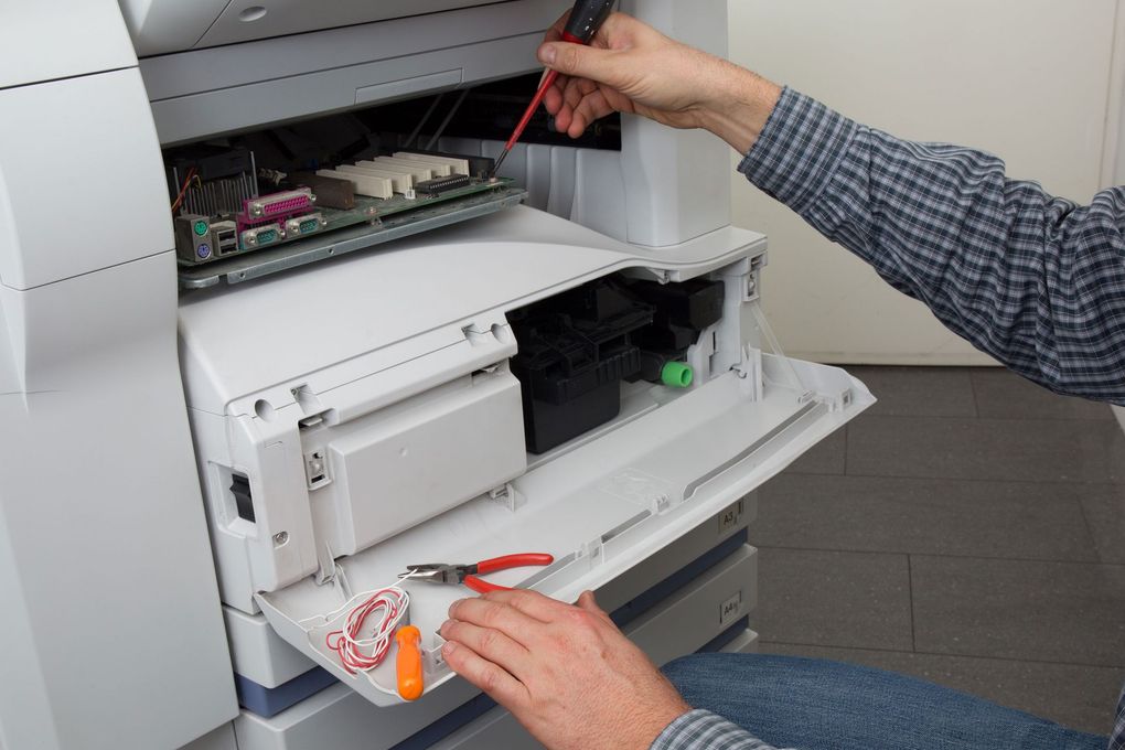 A man is fixing a printer with a screwdriver.