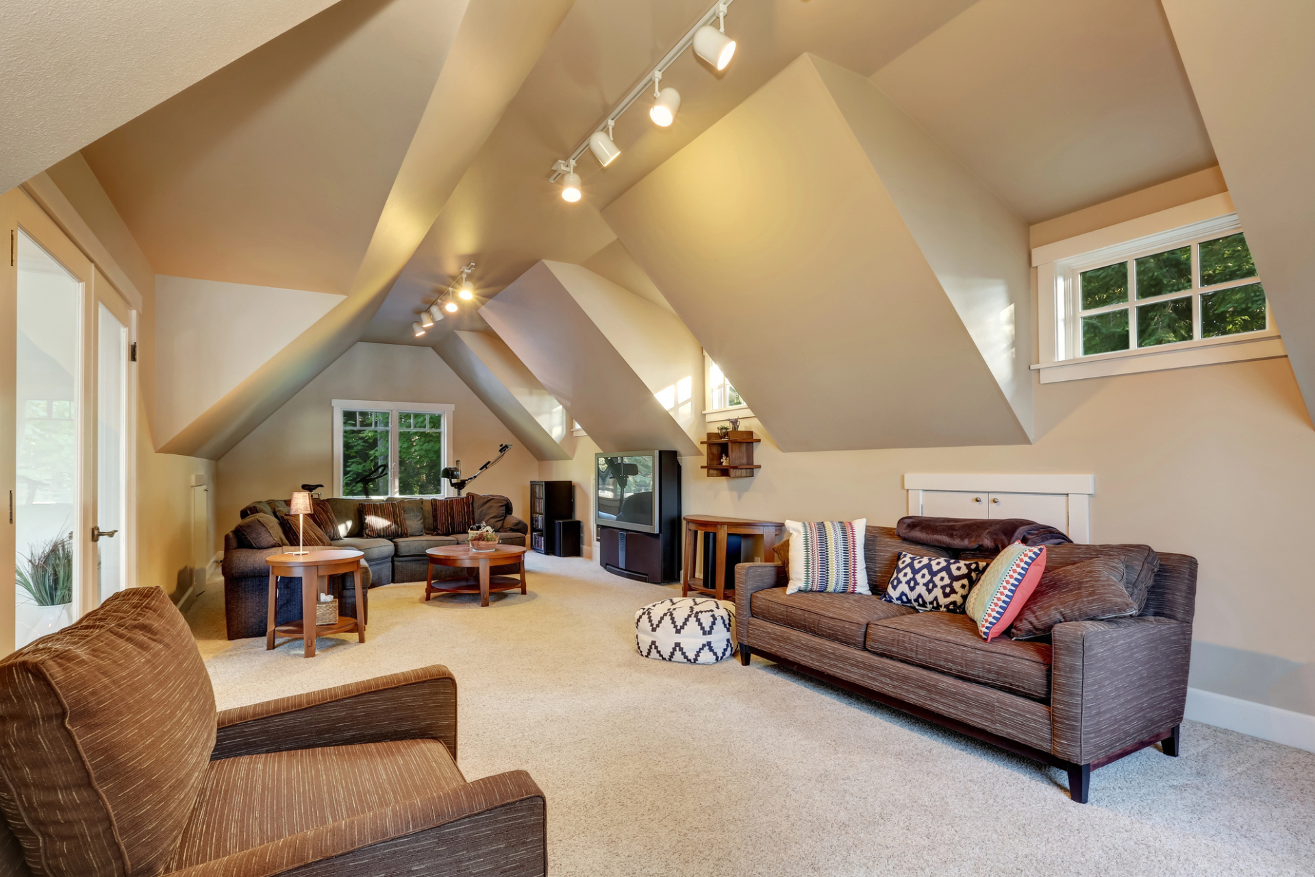 Cozy attic bonus room with sloped ceilings, brown sofas with patterned pillows, and a soft carpet. 