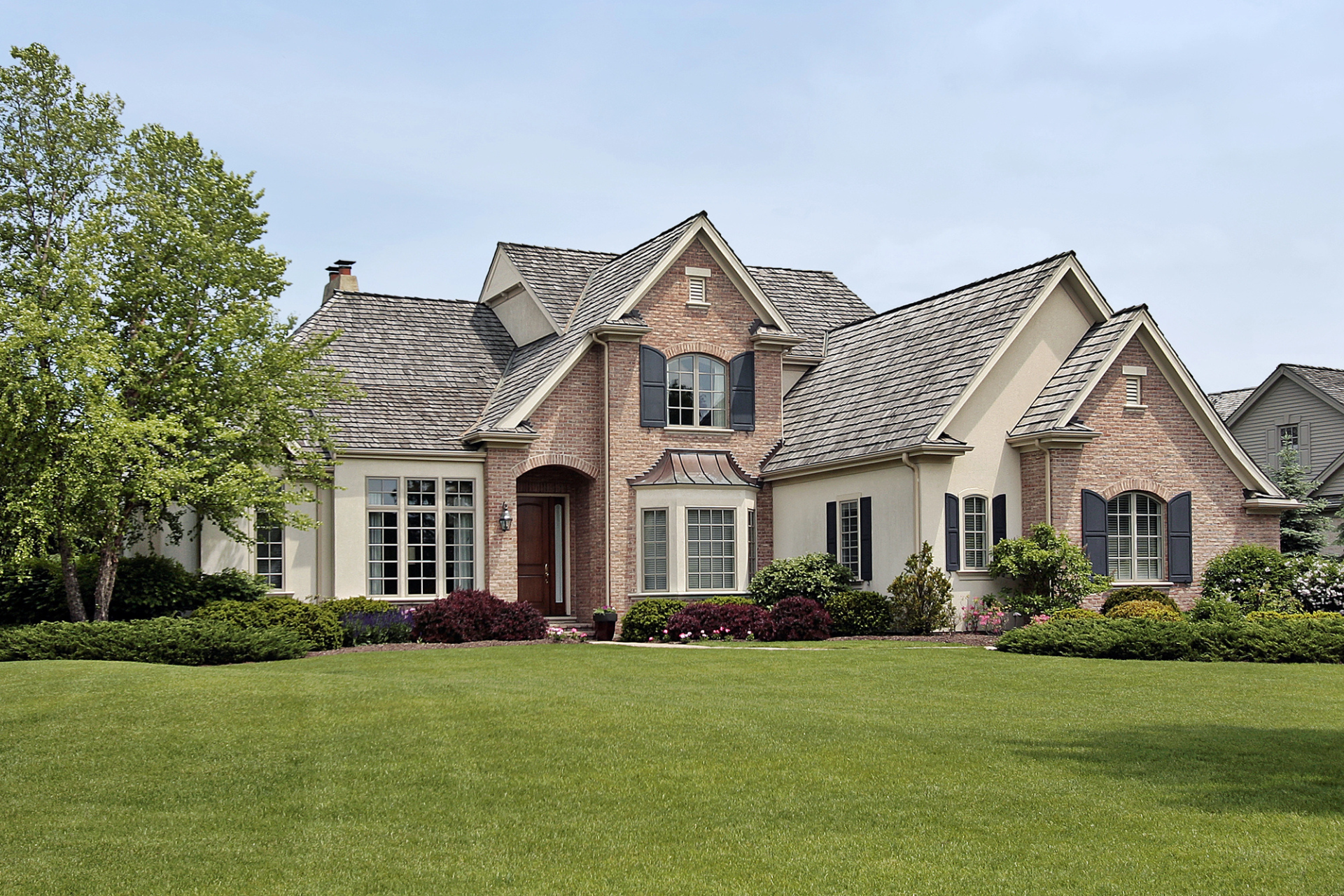 A custom home with brick and cream siding, surrounded by manicured lawns and bushes.