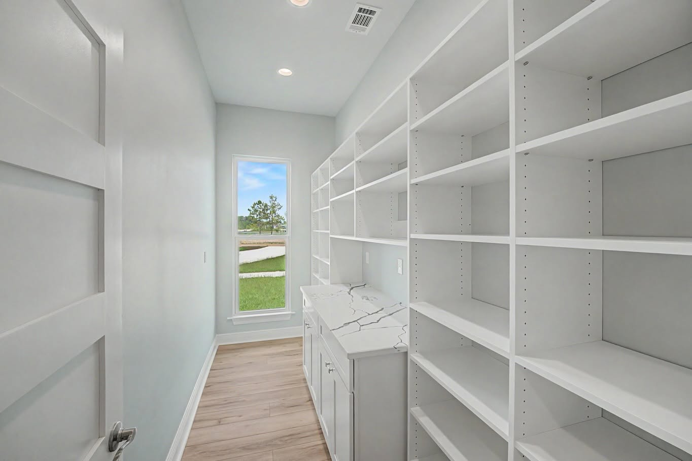 Walk-in pantry with custom shelving, white cabinets and a marble-look countertop