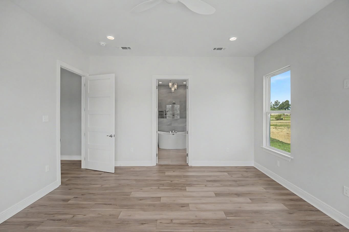 Spacious primary bedroom with wood-look flooring and an adjoining custom bathroom