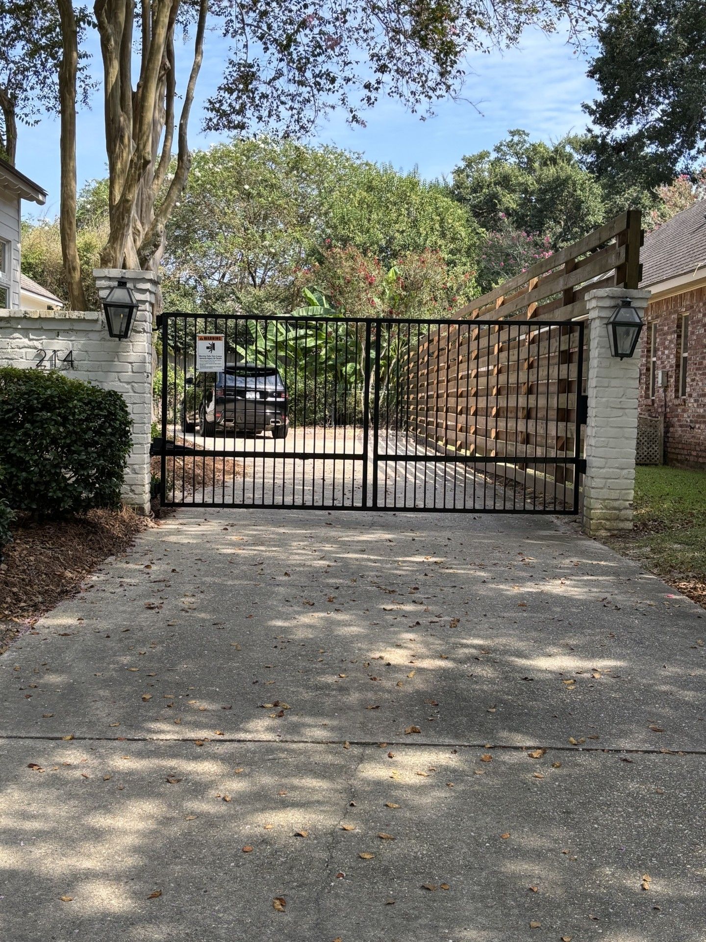 Black wrought-iron fence with arched panels atop a concrete wall, with trees in the background.