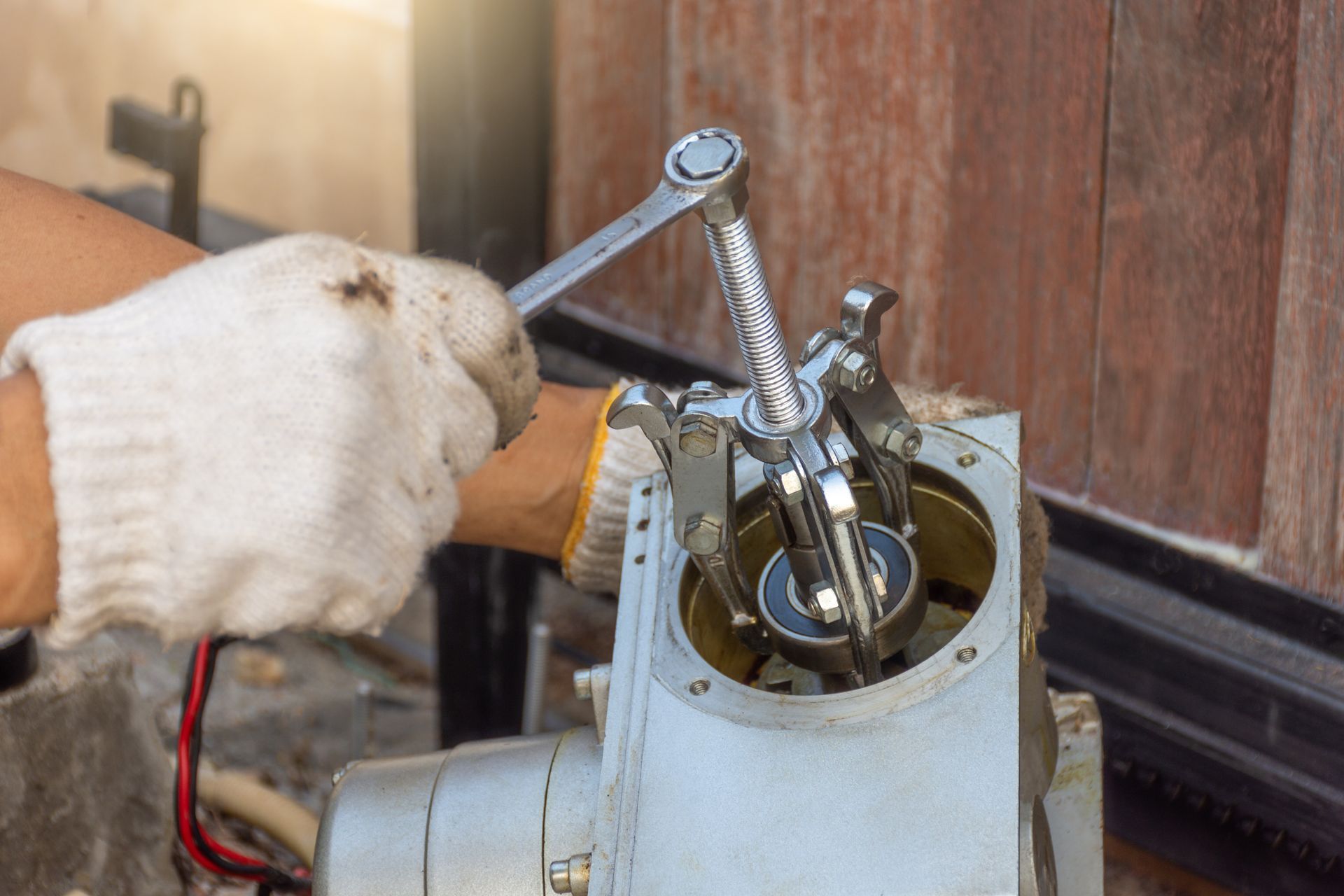 Person in work gloves uses a wrench on an electric gate mechanism.