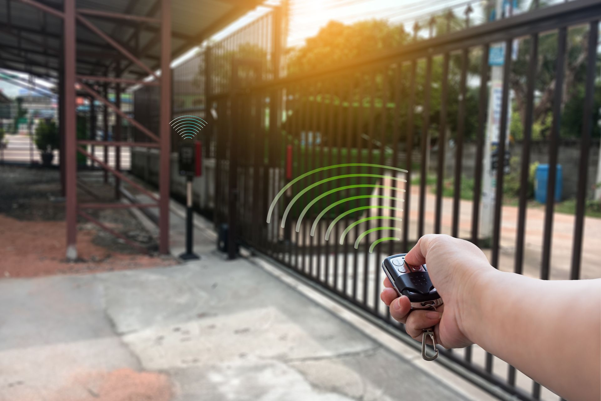 Hand using remote to open a black metal gate. Green signal waves emanate from the remote toward the gate.