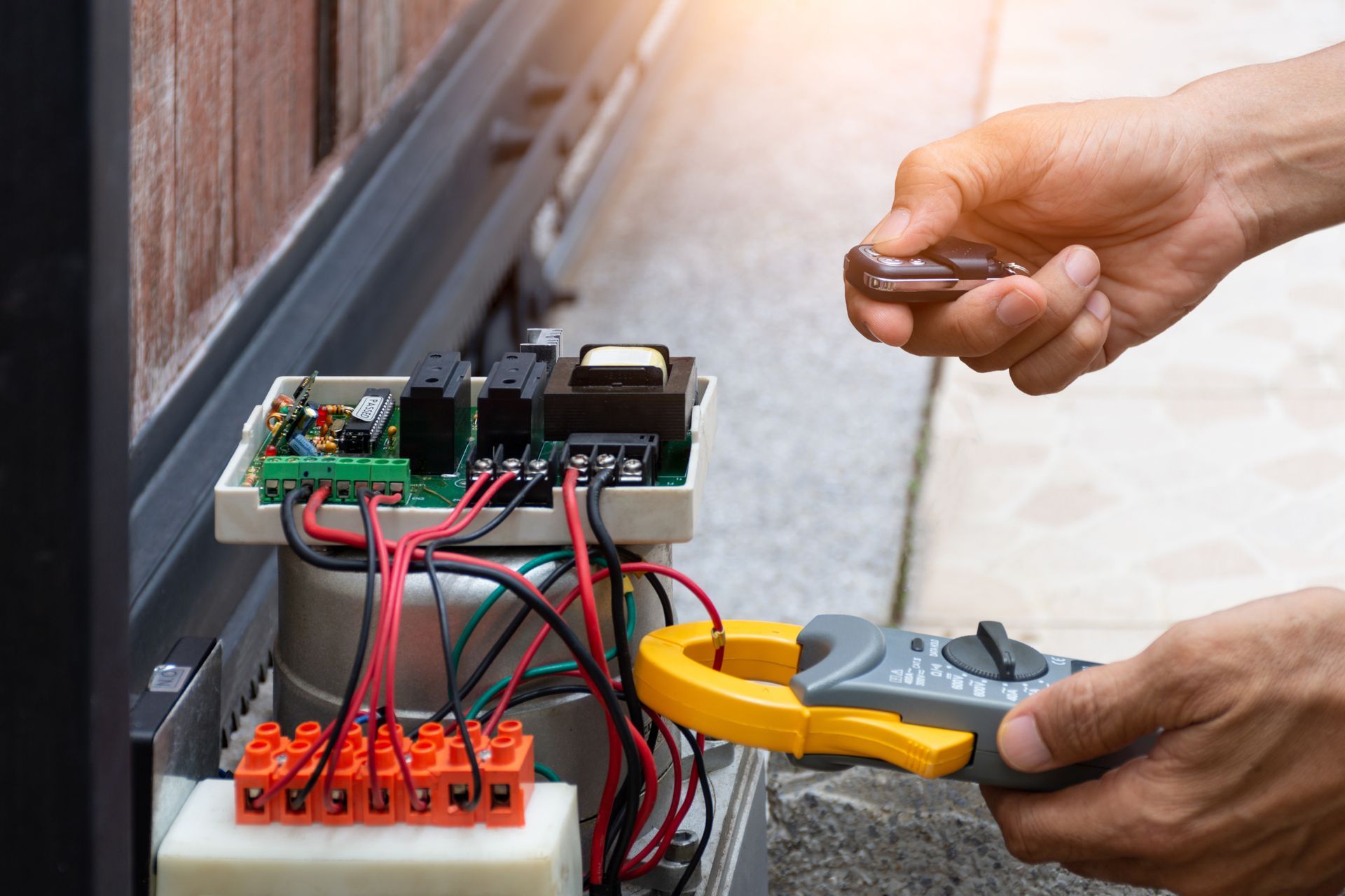 Person repairing a gate opener, using a multimeter and a remote control.