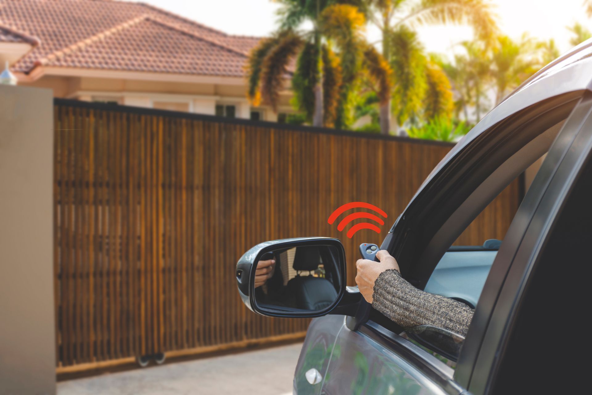 Person in car using remote to open a wooden gate; red signal waves.