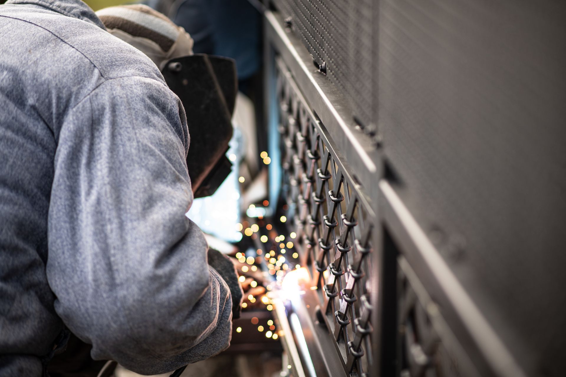 A person welding a metal fence, sparks flying, outdoors.