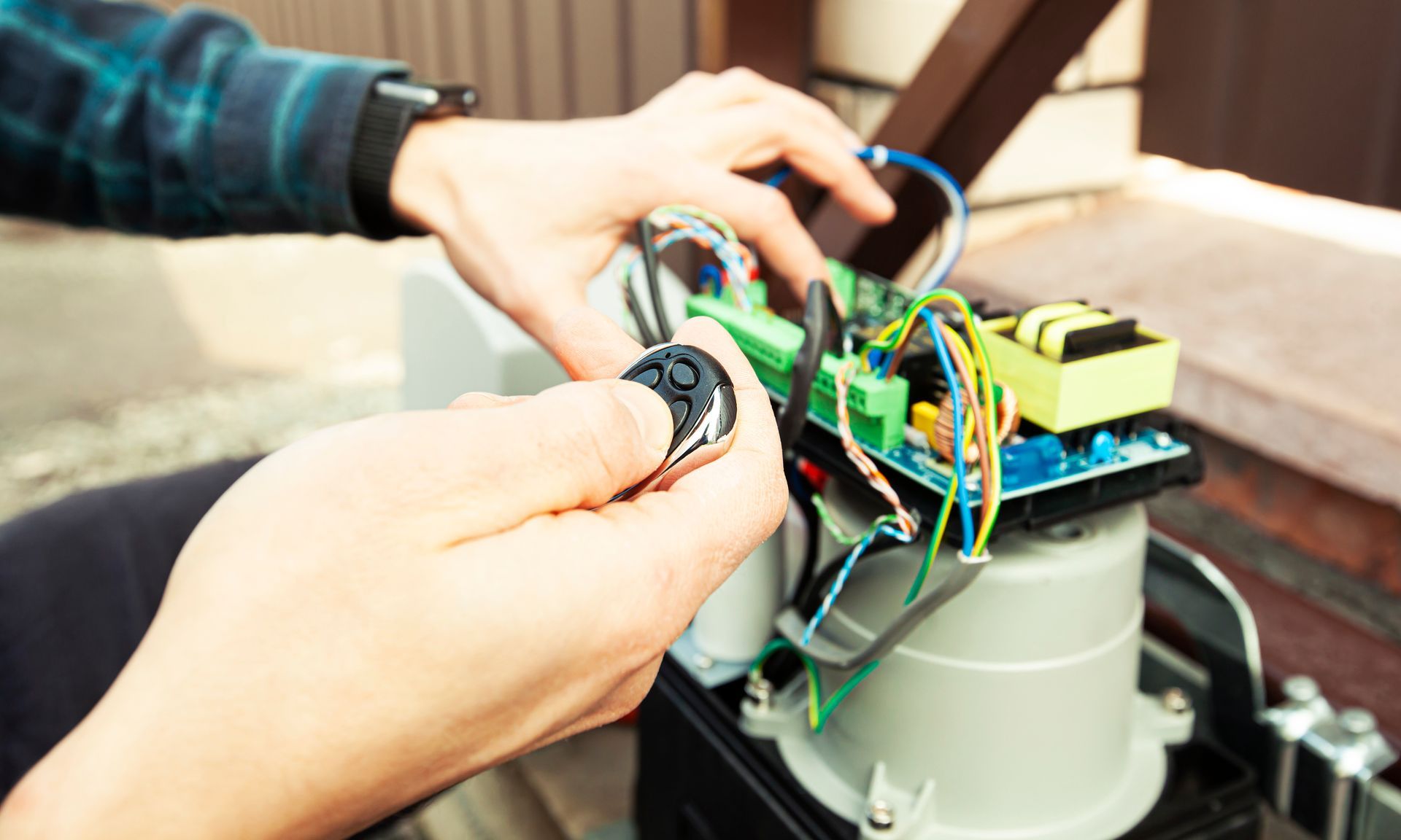 Hands holding a remote near circuit board of an automatic gate opener.