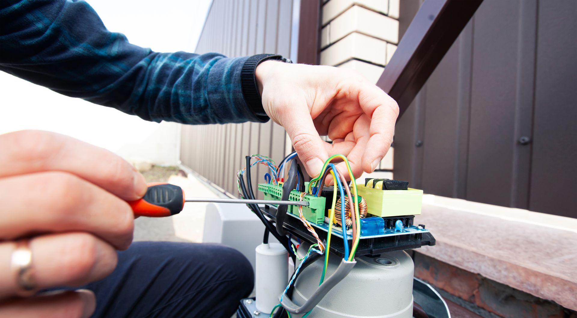 Person using a screwdriver to connect wires on an electronic circuit board, outdoors.