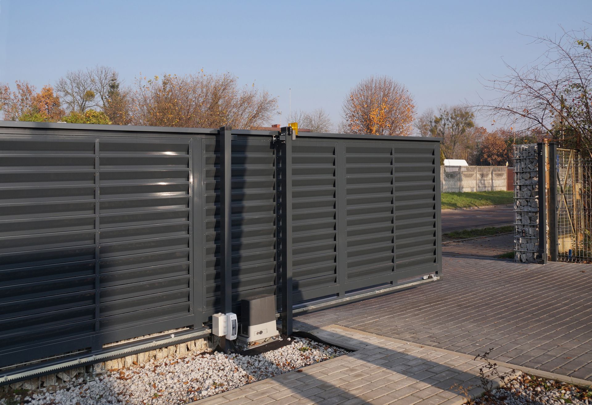 Dark gray sliding gate, partially open, on a paved driveway with gravel.