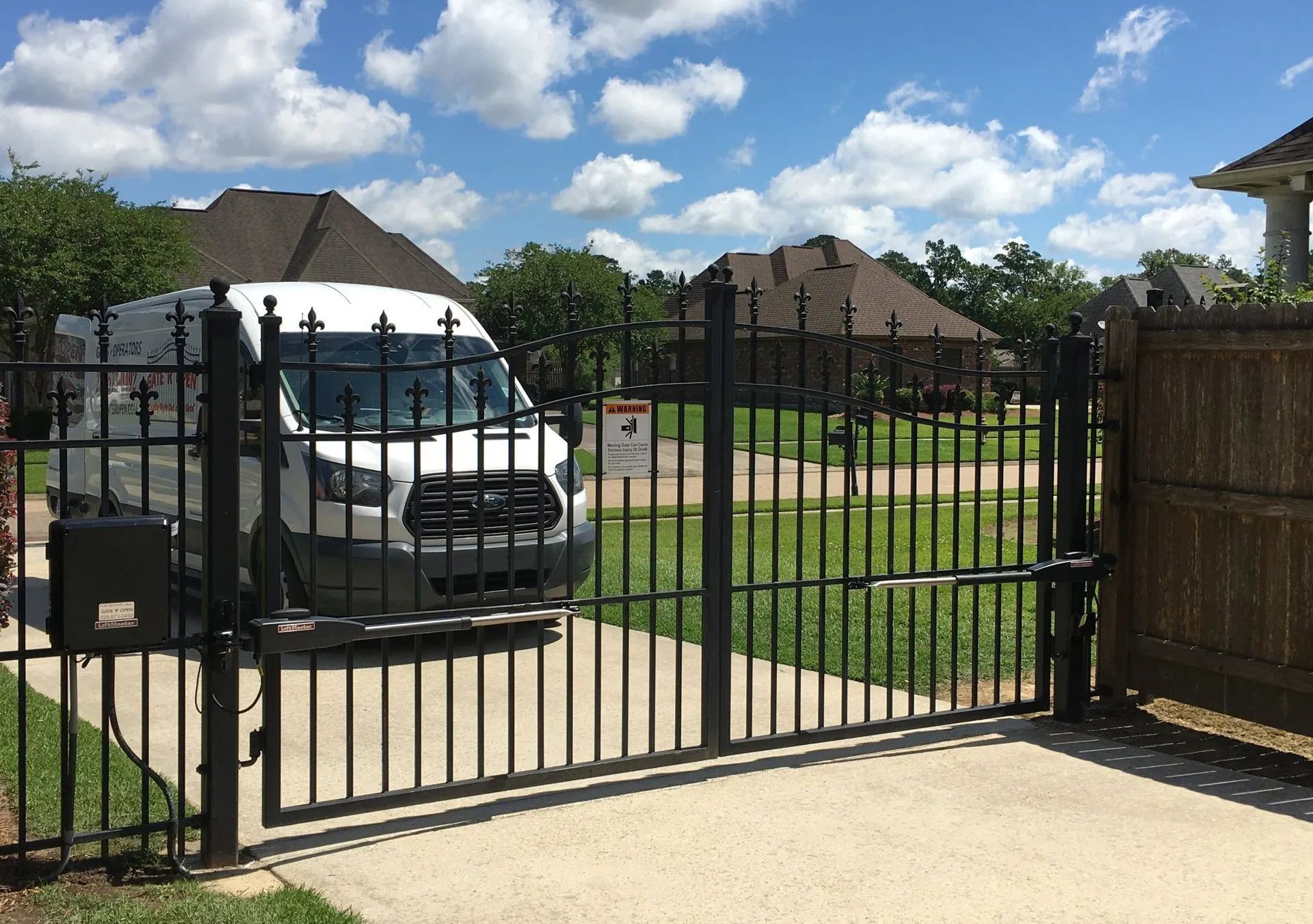White van behind a black metal gate in a driveway. Sunny day, residential setting.