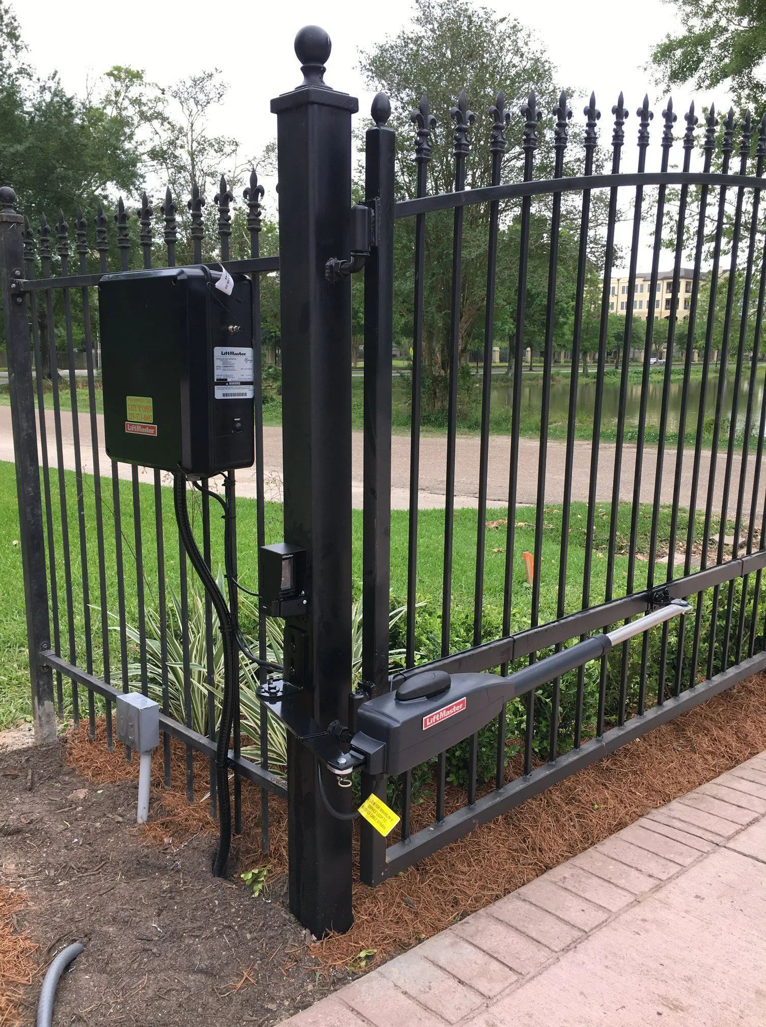 Black metal automatic gate with motor and control box on a black post.