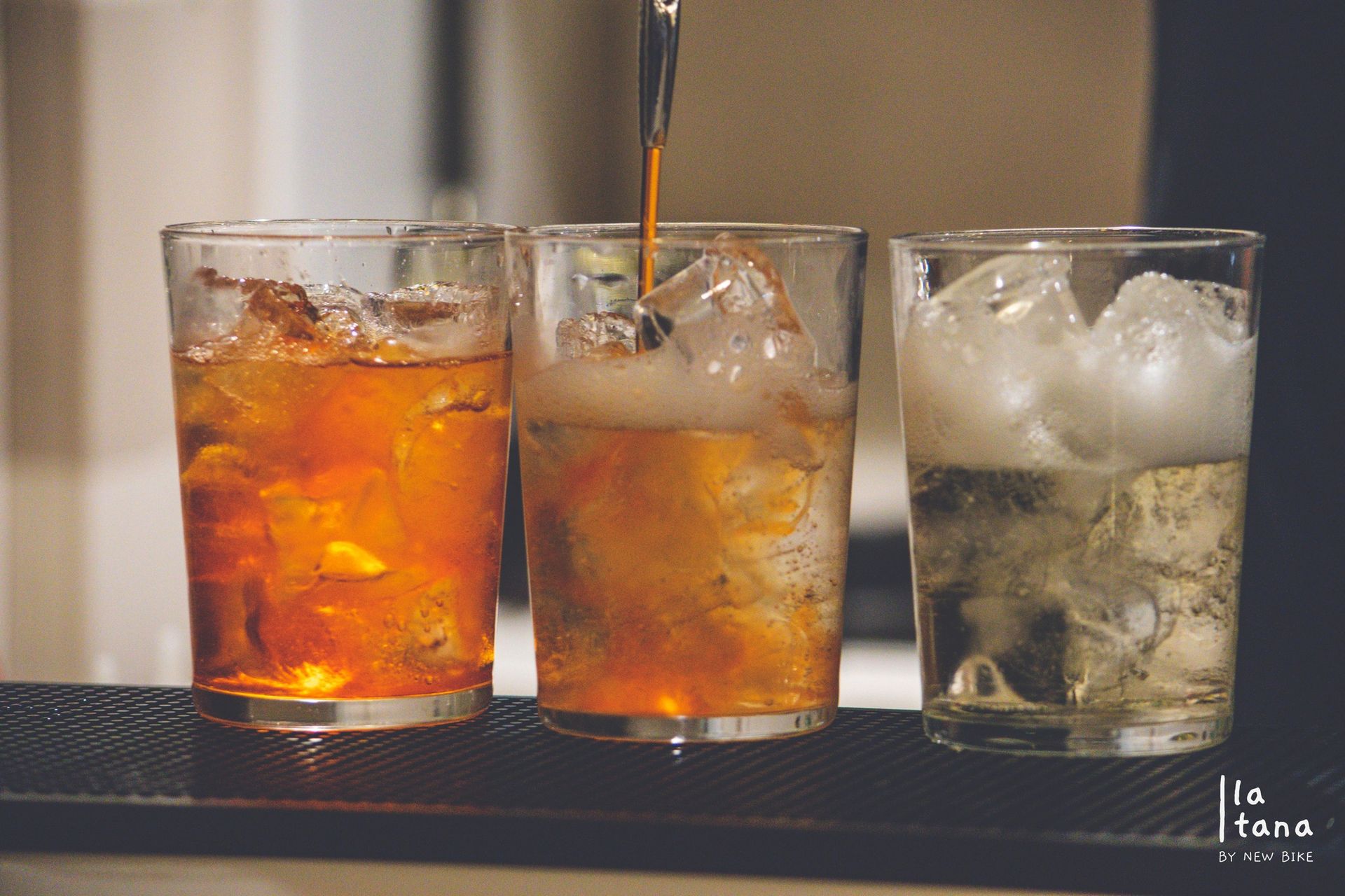 Tre bicchieri pieni di ghiaccio, uno dei quali contenente un liquido color ambra scuro; su un bancone del bar.