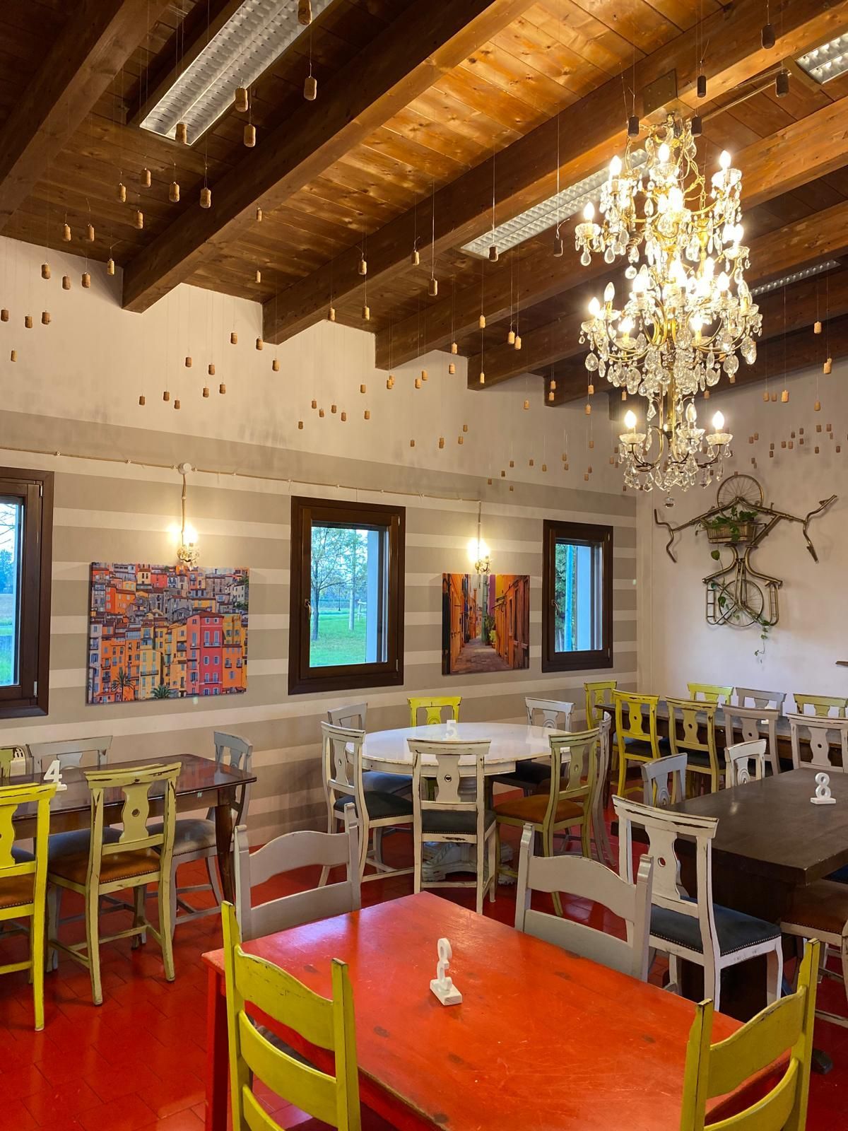 Interno del ristorante con tavoli e sedie colorati, opere d'arte e un lampadario.