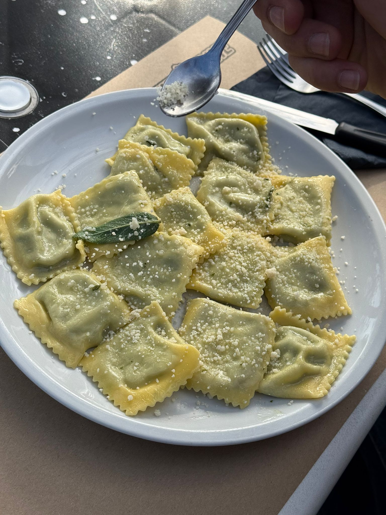Piatto di ravioli al parmigiano, servito su un piatto bianco. Una persona usa un cucchiaio.